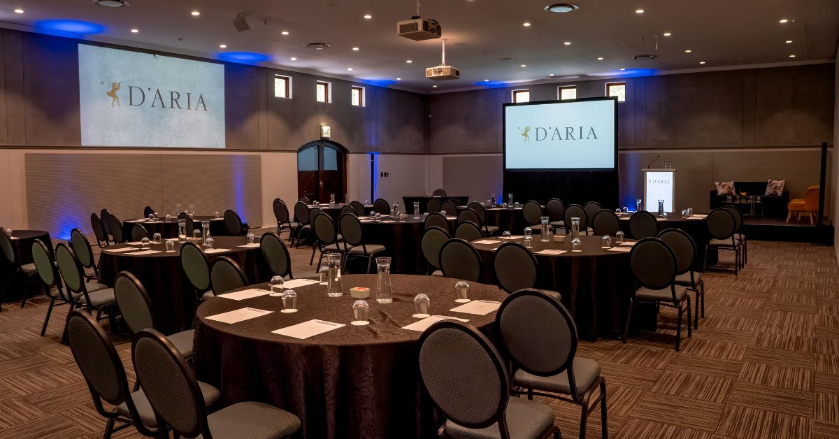 A conference setup in a hall with round tables, chairs and projector screens